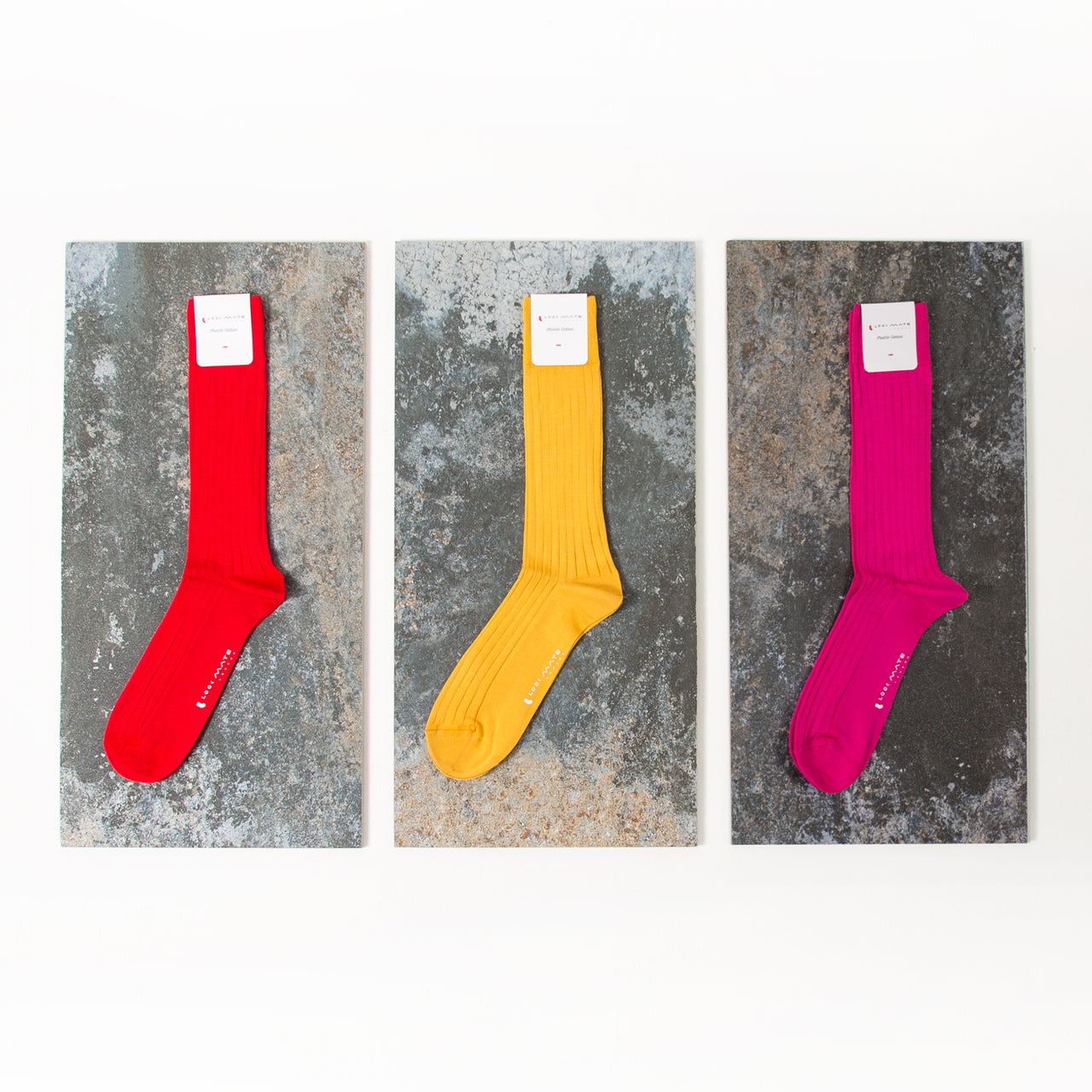 Three pairs of colorful socks (red, yellow, pink) on a textured gray background